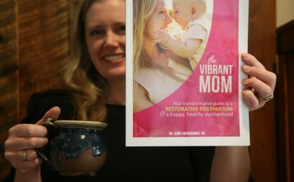 Woman holding tea and "The Vibrant Mom" postpartum recovery guide