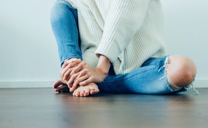 Woman sitting cross-legged on the floor, holding her feet in a posture of reflection and emotional sensitivity