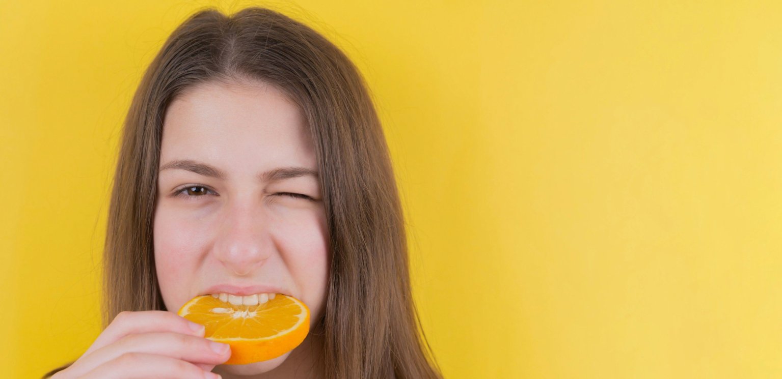 Woman biting a fresh orange slice for radiant skin, symbolizing the link between diet and skin health