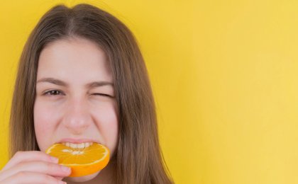 Woman biting a fresh orange slice for radiant skin, symbolizing the link between diet and skin health