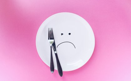 White plate with a sad face and utensils, symbolizing dieting frustration and hormonal weight struggles in women