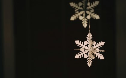 Hanging white paper snowflake against a dark background, symbolizing peaceful holiday simplicity