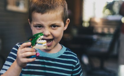 Young boy holding a playful alligator toy and smiling wide, showing teeth