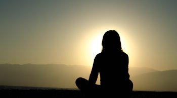 Woman meditating at sunrise on the beach, symbolizing nervous system calm and healing