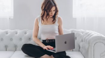 Woman sitting on a couch with a laptop open on her lap, reading in a relaxed home setting.