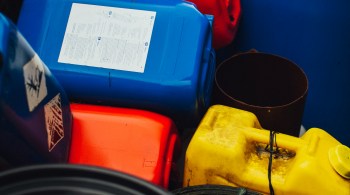 A pile of stacked red gasoline containers, representing the everyday environmental and chemical exposures — fuels, solvents, industrial compounds — that the body processes through its liver detox pathways; used to illustrate the genetics of liver detox and how exposure load interacts with individual detox capacity.
