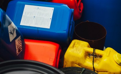 A pile of stacked red gasoline containers, representing the everyday environmental and chemical exposures — fuels, solvents, industrial compounds — that the body processes through its liver detox pathways; used to illustrate the genetics of liver detox and how exposure load interacts with individual detox capacity.
